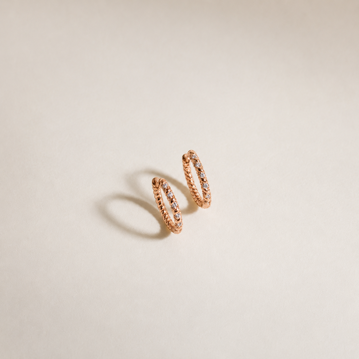 Rose gold hoop earrings with embedded stones on a beige background